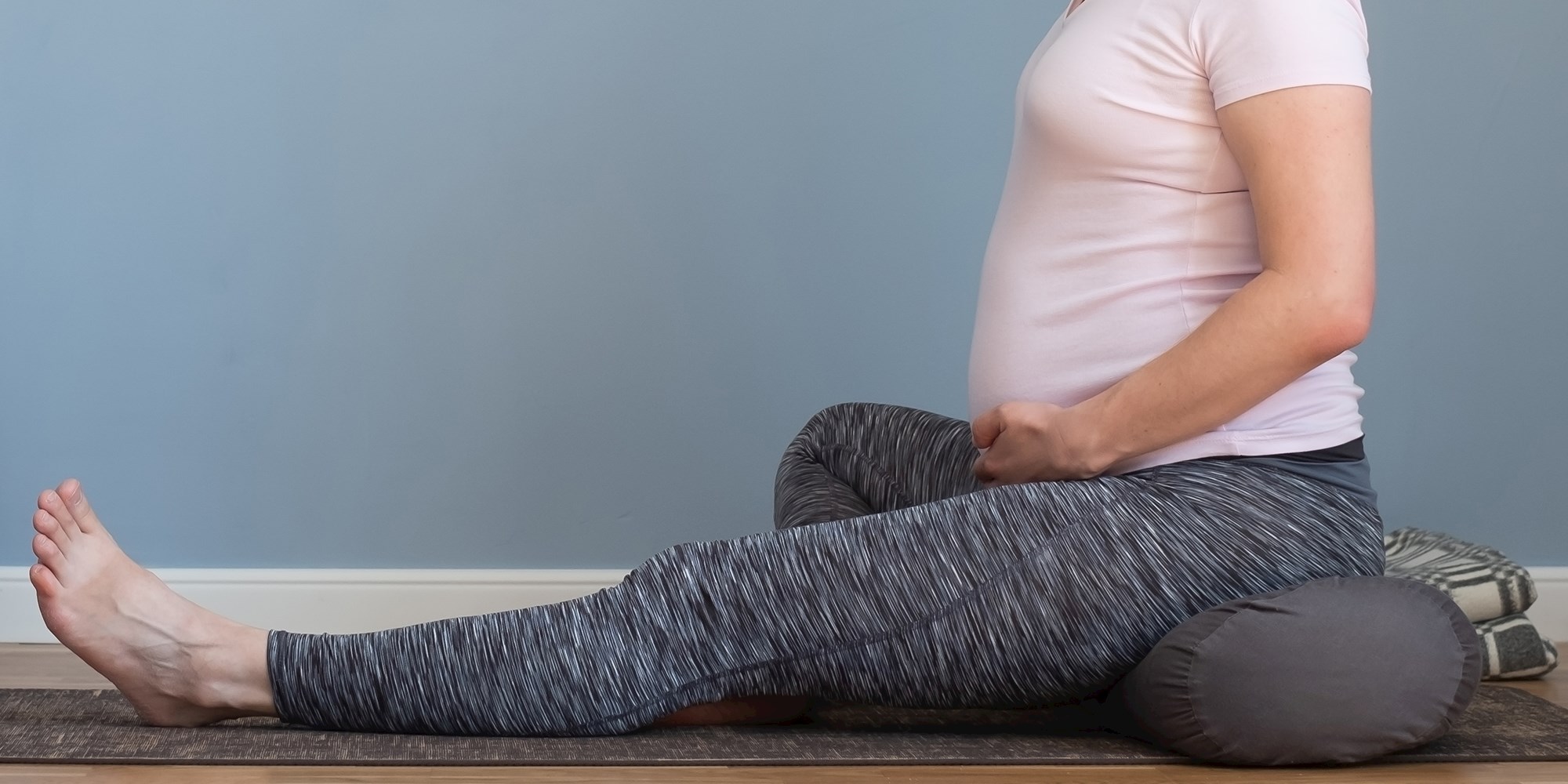 Gravid kvinde der sidder på en yogapølle og yogamåtte i behageligt træningstøj