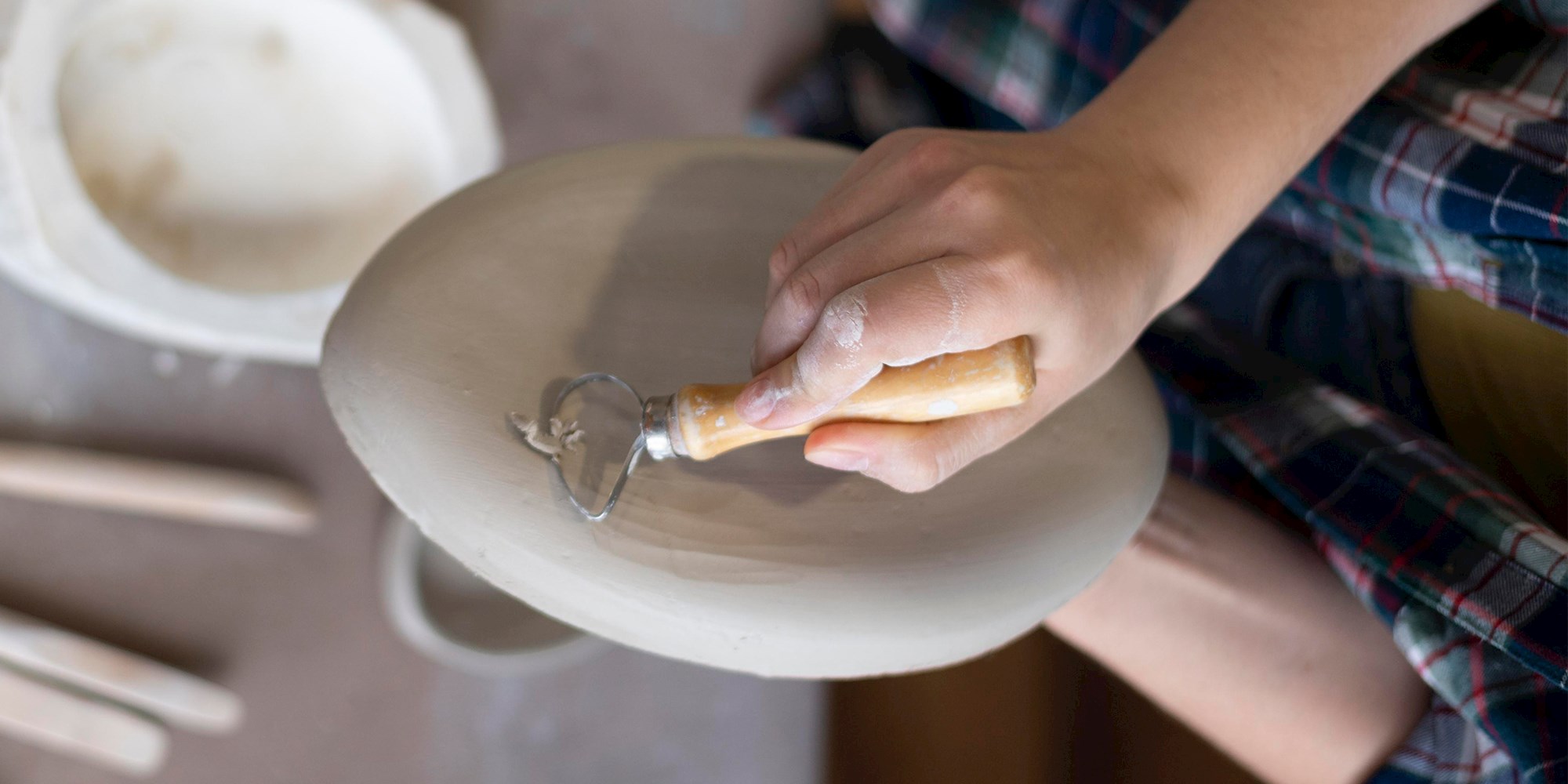 Barn, der skærer i en lerform over et bord med et keramikværktøj