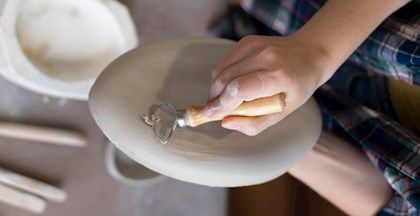 Barn, der skærer i en lerform over et bord med et keramikværktøj