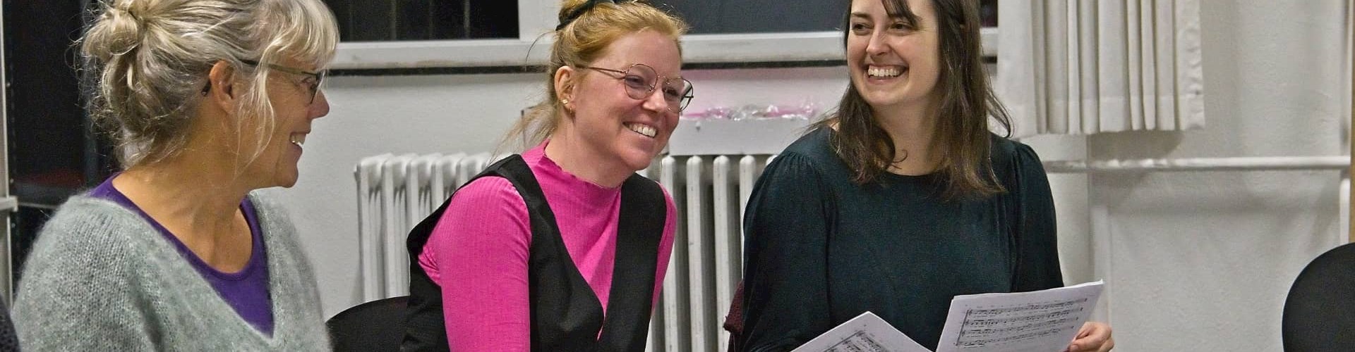 Kvinder smiler med nodeark i hånden til sangundervisning i FOF Aarhus