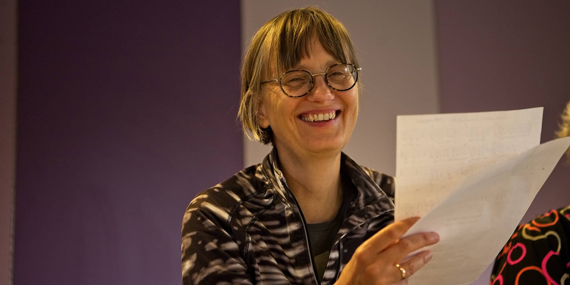 Kvinde der griner med nodeark i hånden til kursus ved FOF Aarhus