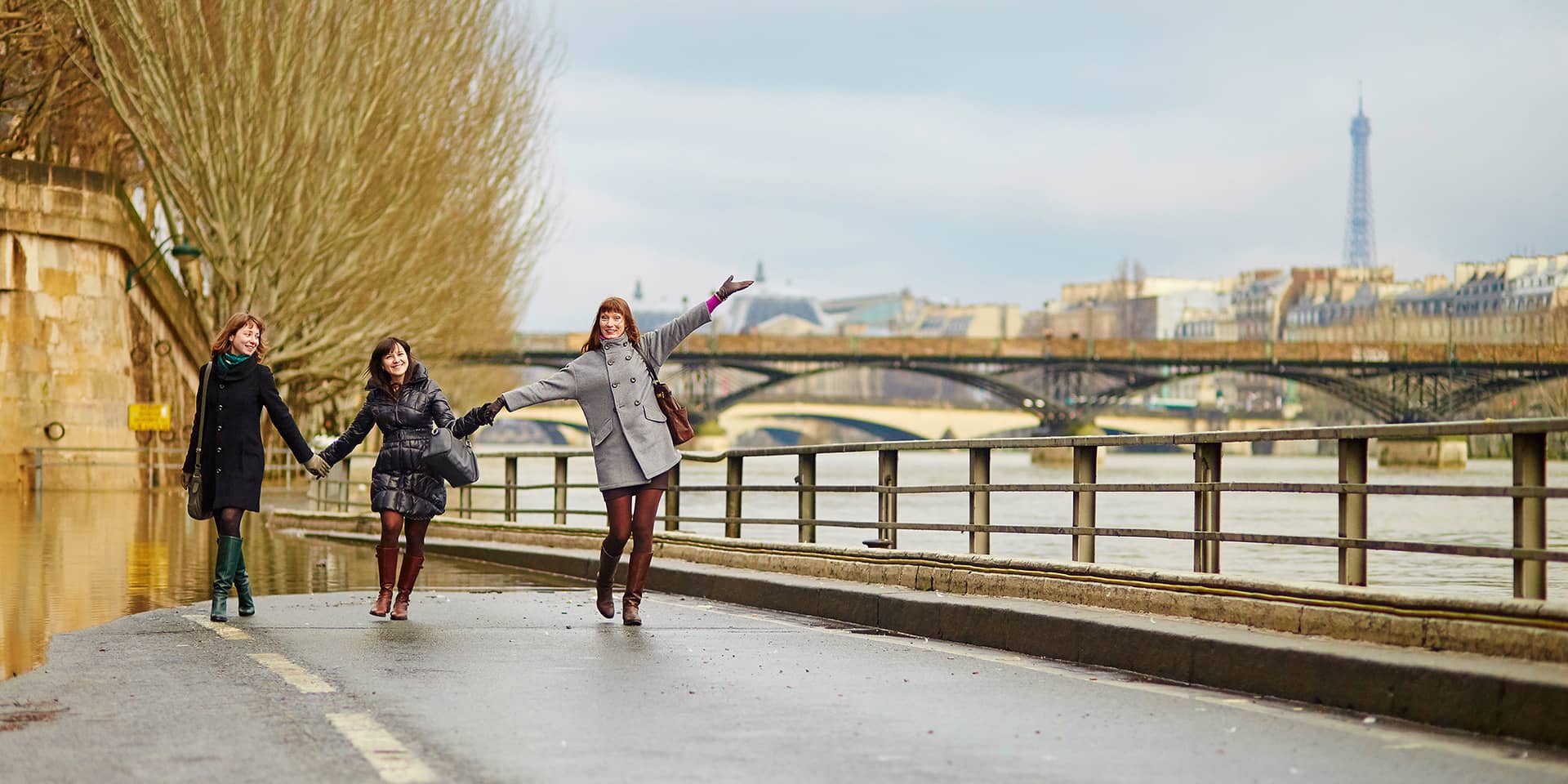 Billede af tre kvinder på en bro i Paris, med Eiffeltårnet i horisonten
