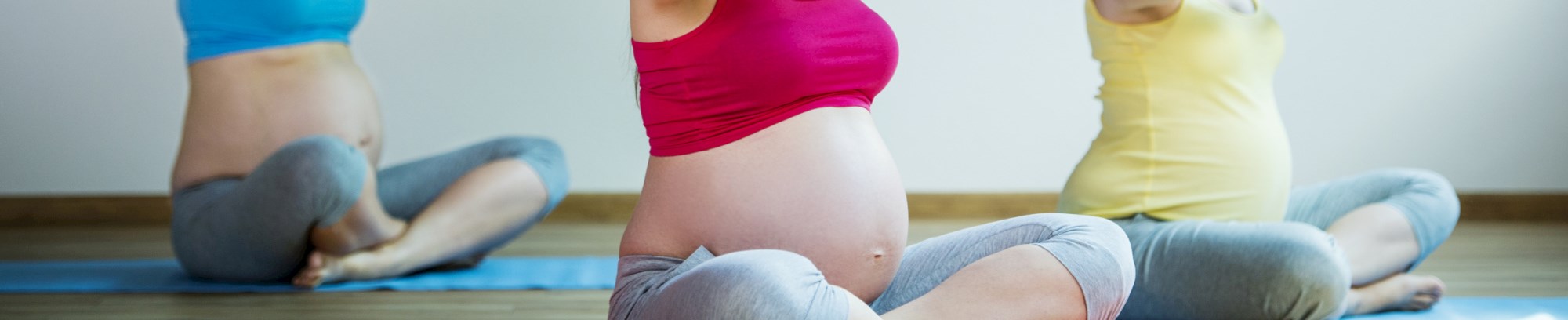 Tre højgravide kvinder laver yoga på måtter