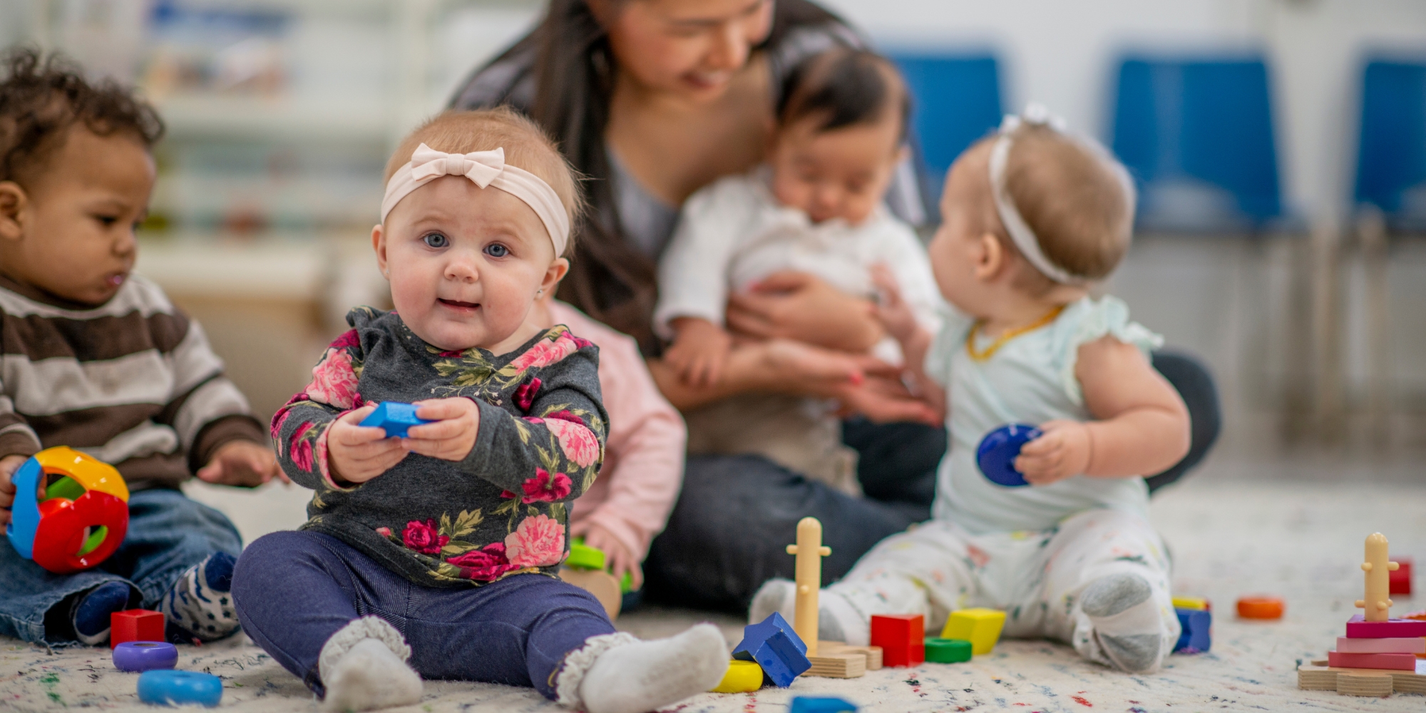 Babyer på gulv med legetøj og en voksen