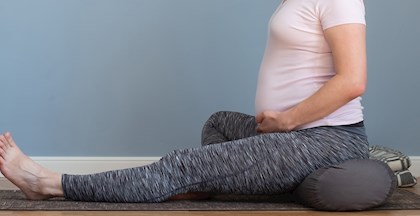 Gravid kvinde der sidder på en yogapølle og yogamåtte i behageligt træningstøj