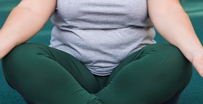 Overvægtig kvinde sidder med benene over kors på en yoga måtte og slapper af