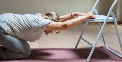 Senior der laver strækøvelser med stol på en yogamåtte