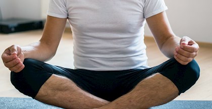Mand der sidder med benene over kors og laver en rolig åndedræts øvelse på en yoga måtte