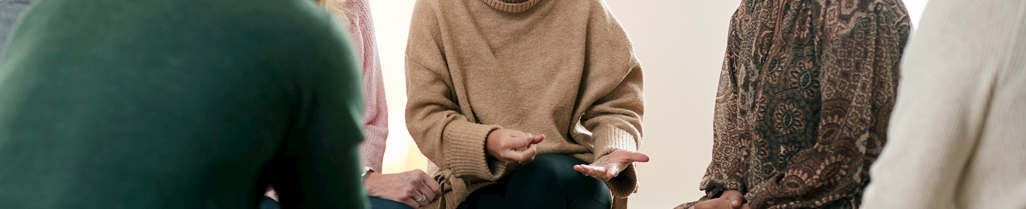 Personer fra forskellige baggrunde og i forskellige aldre, der sidder sammen i en rundkreds og lytter til en ung dame der fortæller