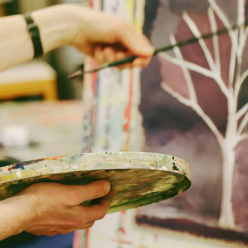 hænder i gang med at male på lærred med pensel - i Malersalen hos FOF i Randers