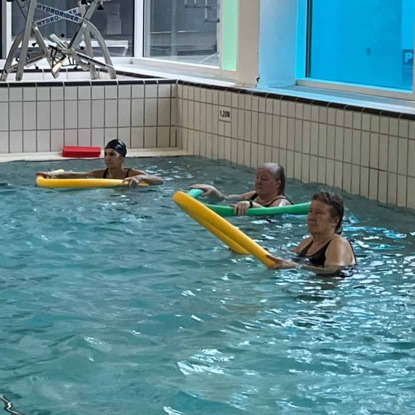 Kursister der laver øvelser i vandbassin i en svømmehal iført badedragter