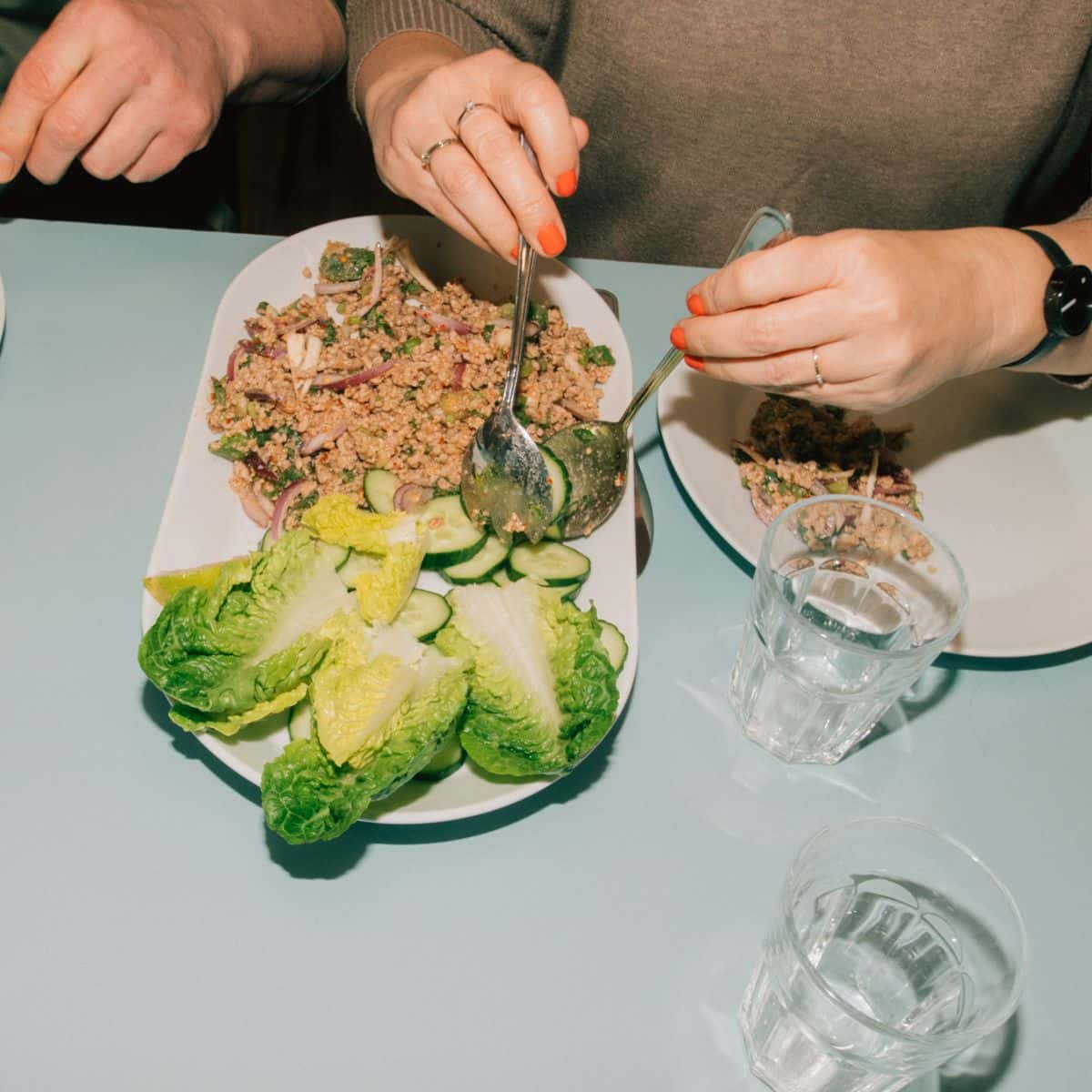 Person anretter thailandsk mad med friske grøntsager og krydret kød på tallerken – stemning af fællesskab og madglæde