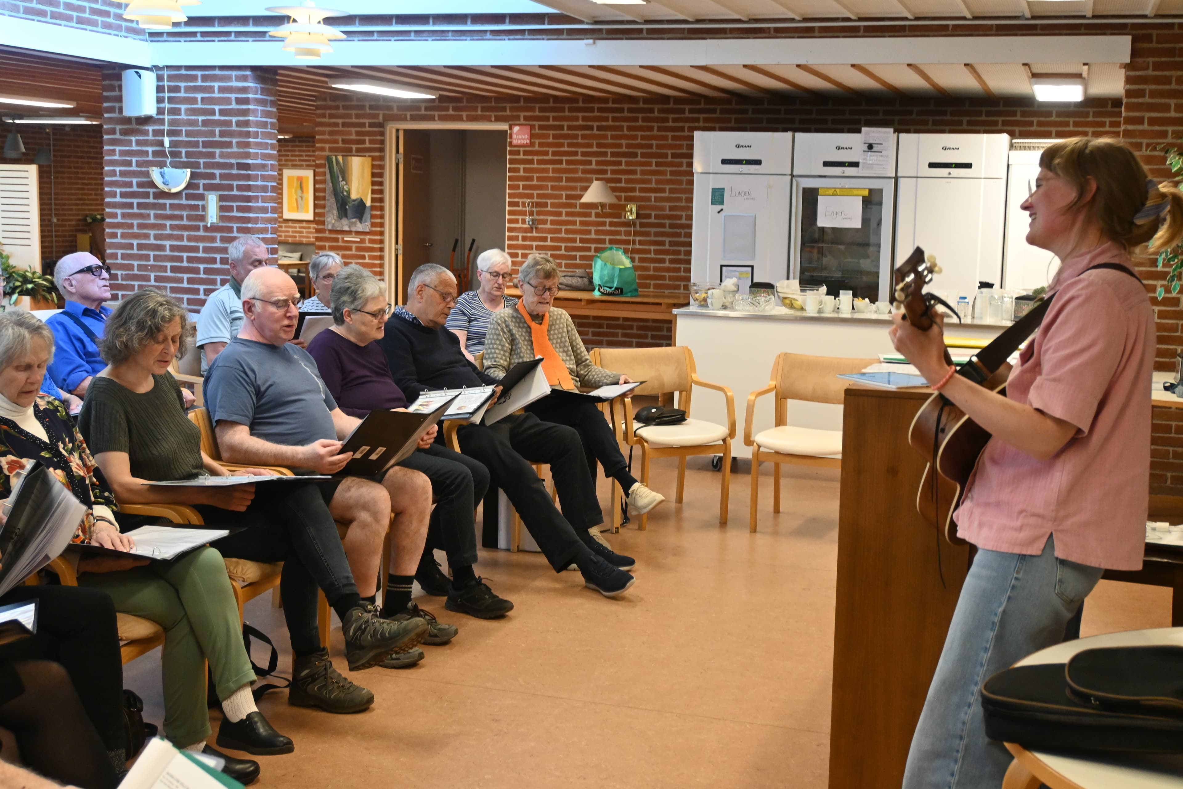 Underviser synger med kor og spiller guitar