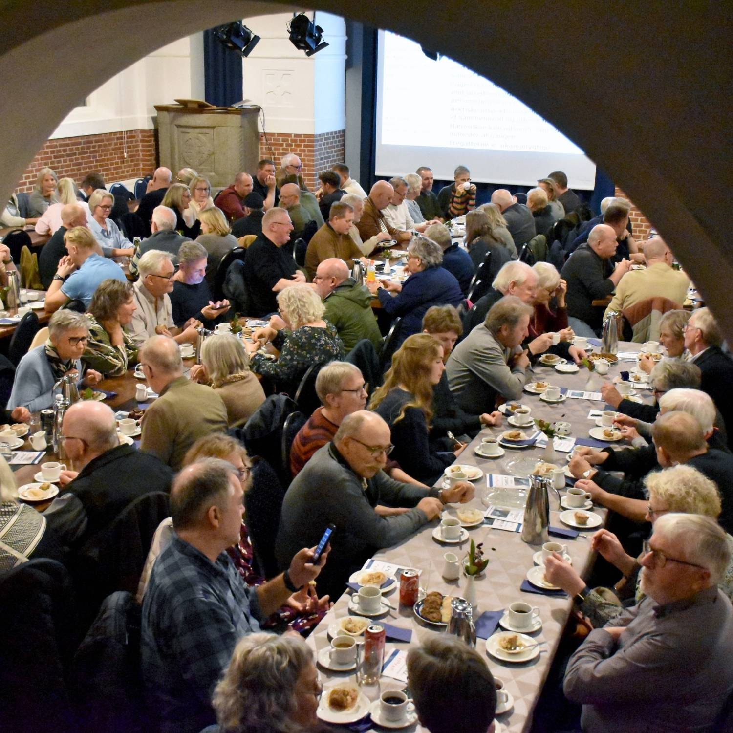 Deltagere der spiser sammen ved langborde inden foredrag på Emanuel i Skærbæk