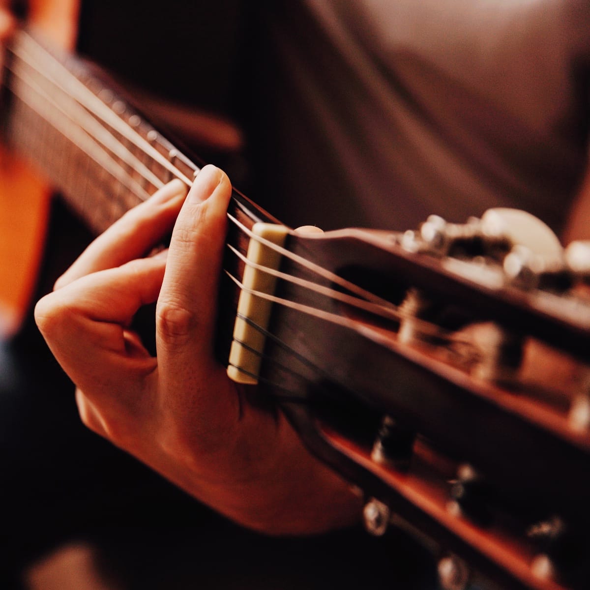 Person spiller på akustisk guitar – fokus på hånd og gribebræt, symbol på musik og sammenspil.