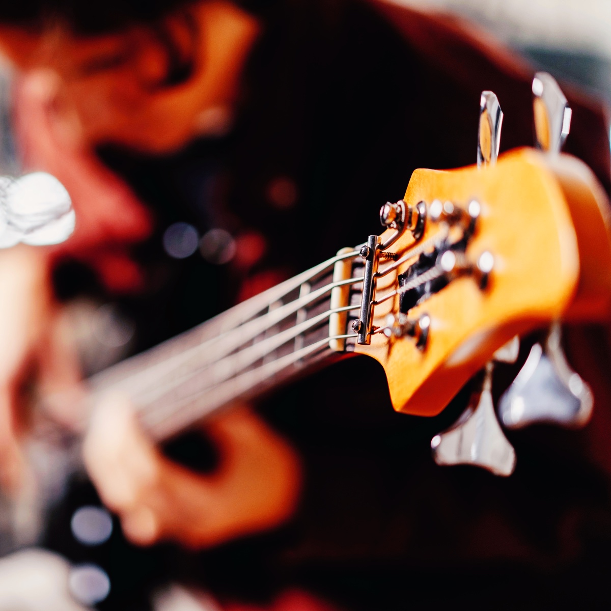 Person spiller på elbas – fokus på instrumentets hoved og strenge, symbol på rytmisk musik og sammenspil.