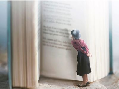 En meget lille kvinde med hat står og læser i en bog, der er større end hende