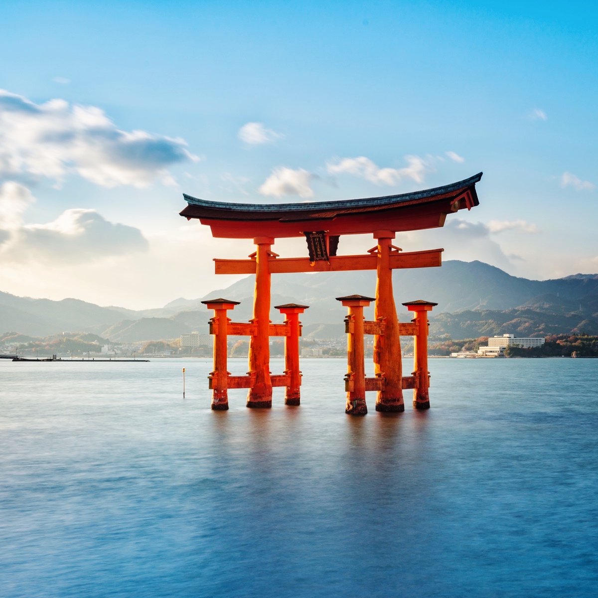 Rød japansk torii-port i vandet med bjerge i baggrunden.