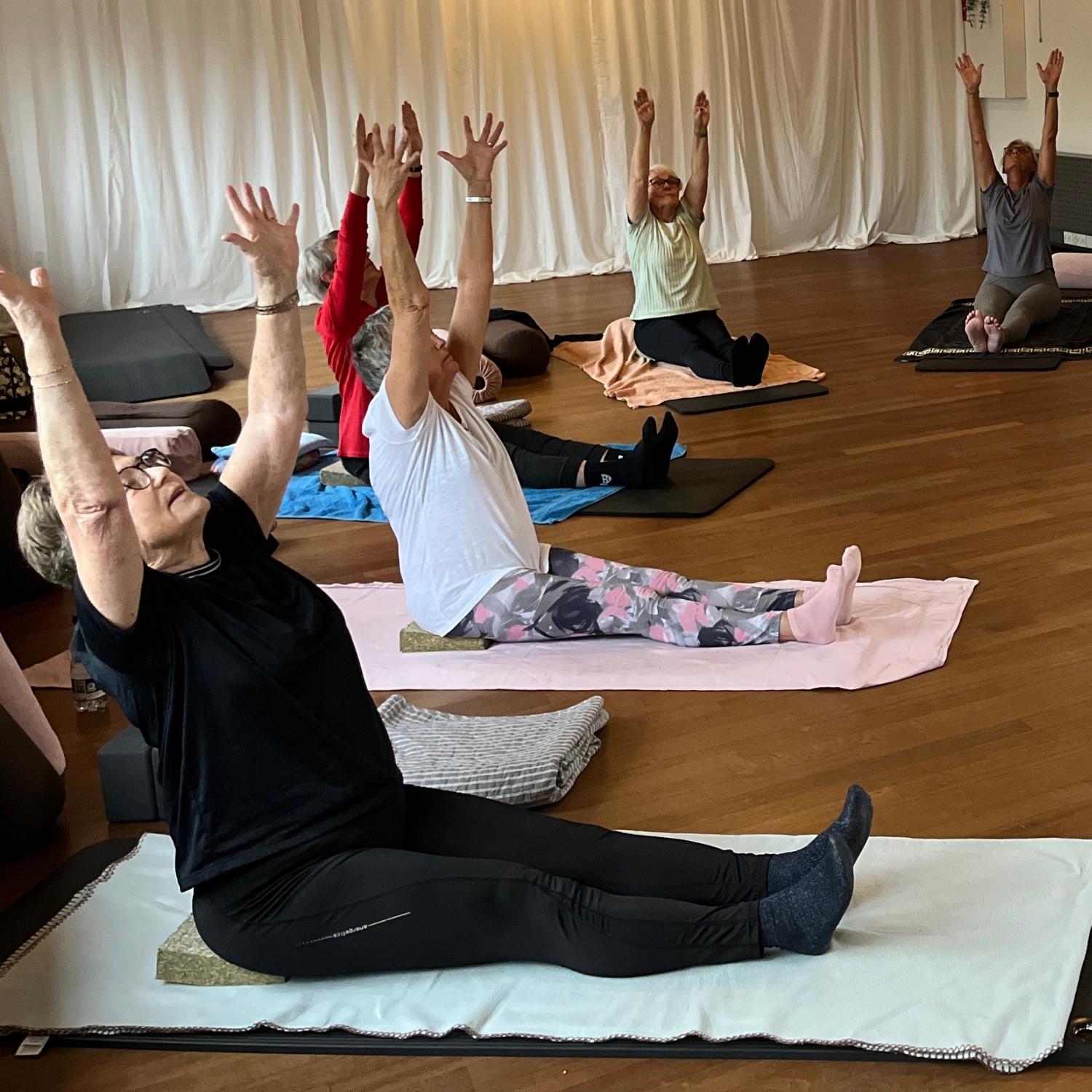 Kursister der laver skånsomme yoga øvelser på yogamåtter i afslappet træningstøj