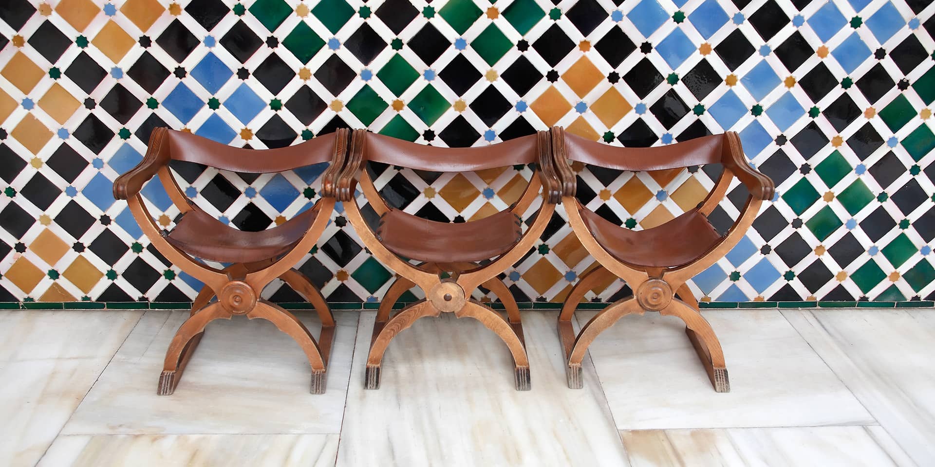 Billede af tre stole ved flisevæg i Granada, Spanien. Kom på spanskkursus i FOF Aarhus: Spansk 3 (A1-A2)