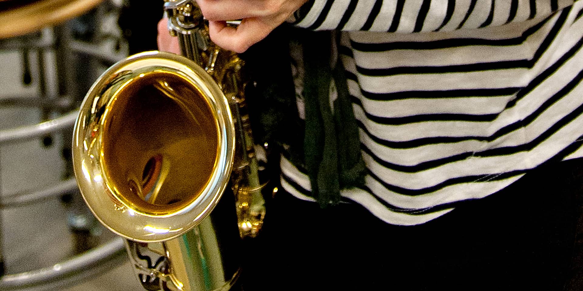 Et udsnit af en saxofon og en person med en stribet bluse. På kursus i saxofon for nybegyndere i FOF Aarhus.