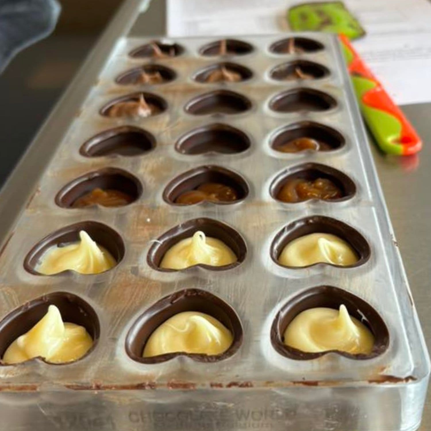 Støbeform til fyldte chokolader, der har fået chokolade og cremet fyld i flere varianter