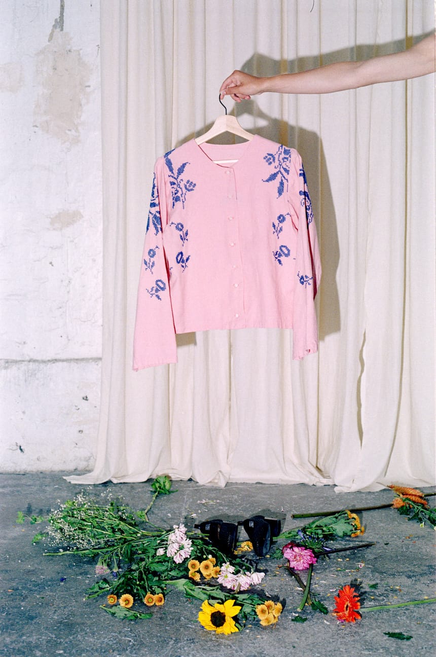 Pink shirt with blue embroidery held up above scattered flowers