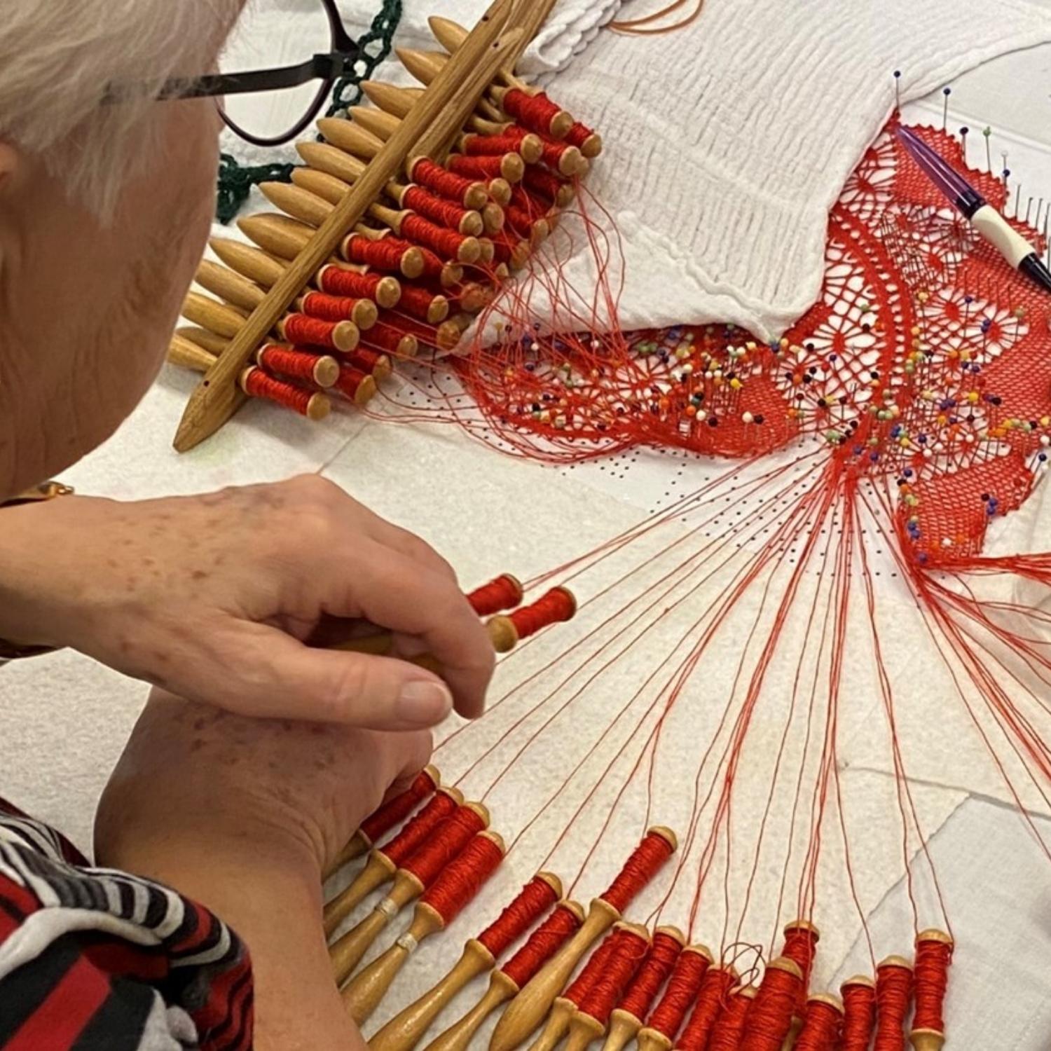 Kursist der knipler med rød tråd på et kniplebræt