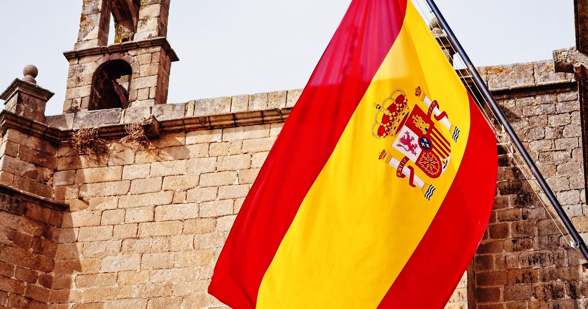 Spansk flag foran historisk bygning – symbol på sprog og kultur.”