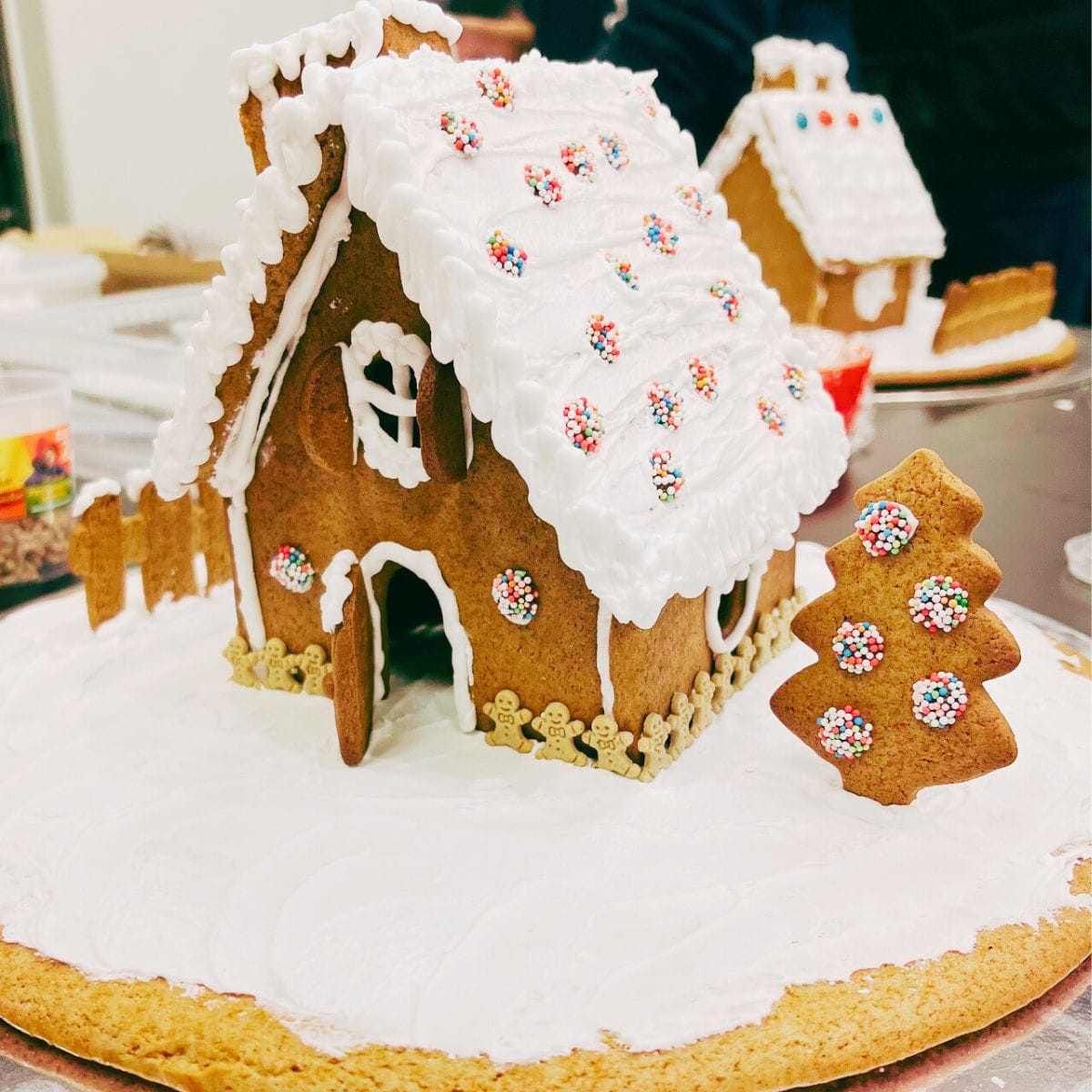 Deltager dekorerer et brunkagehus med glasur og fondant i julefarver under et julekursus