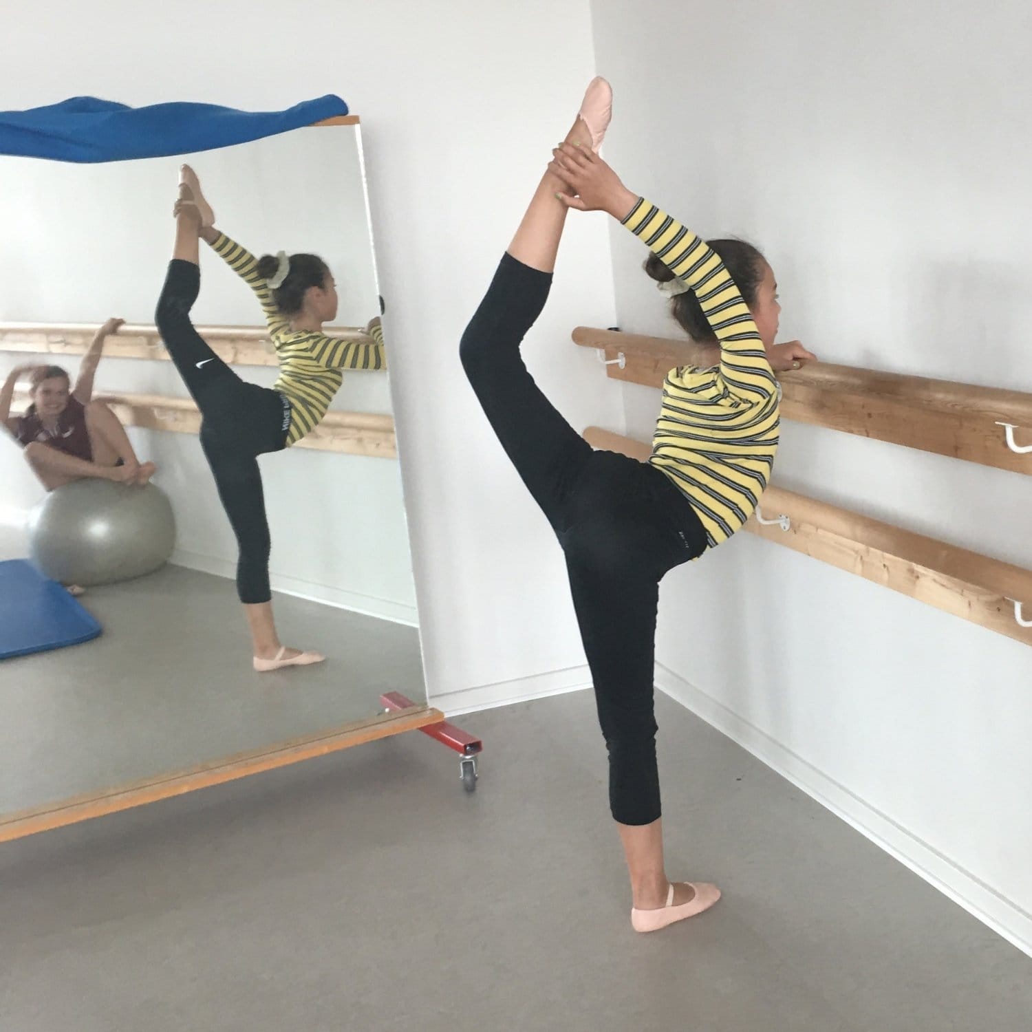 Balletbarn der laver øvelser ved en barre og et spejl