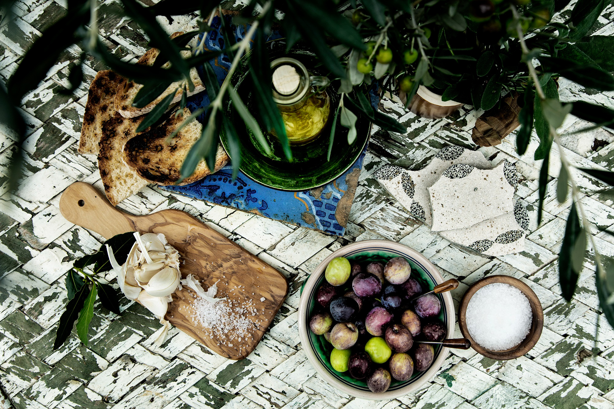 Rustikt bord med frisk olivenolie, brød, hvidløg og oliven