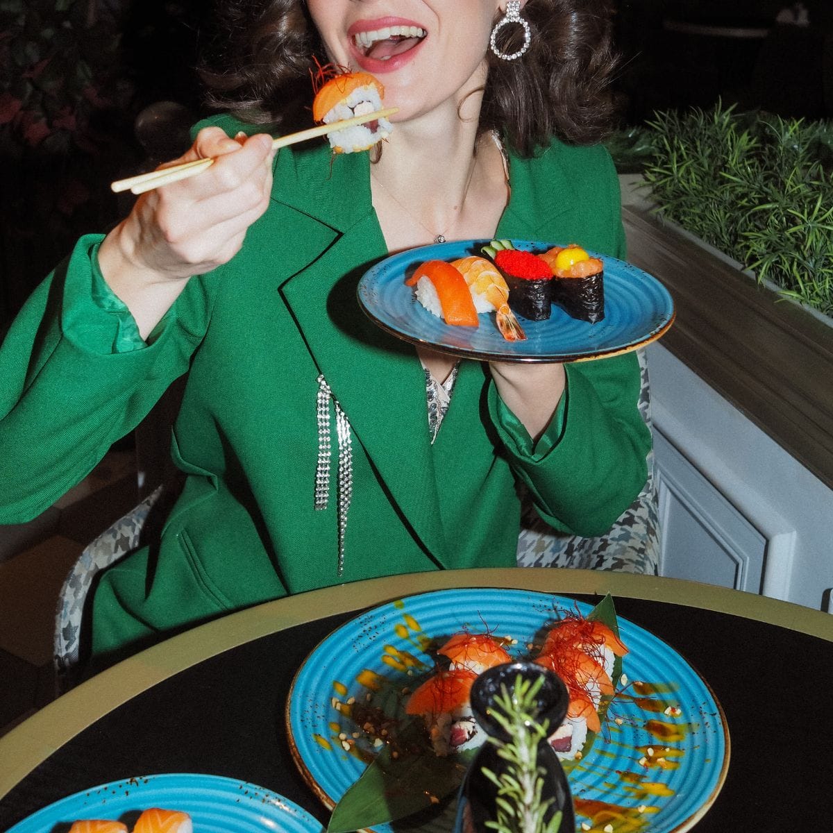 En kvinde i grøn jakke der sidder og spiser sushi