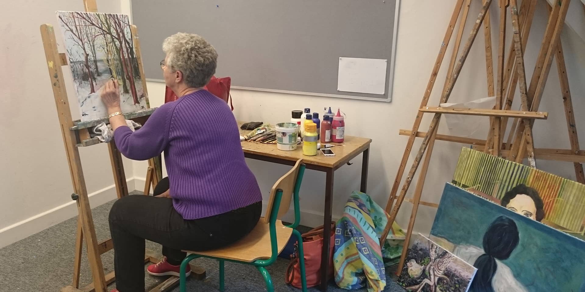 En kvinde, der maler et billede, der står på et staffeli, til malekursus i FOF Aarhus: maleværksted og kunstforståelse.