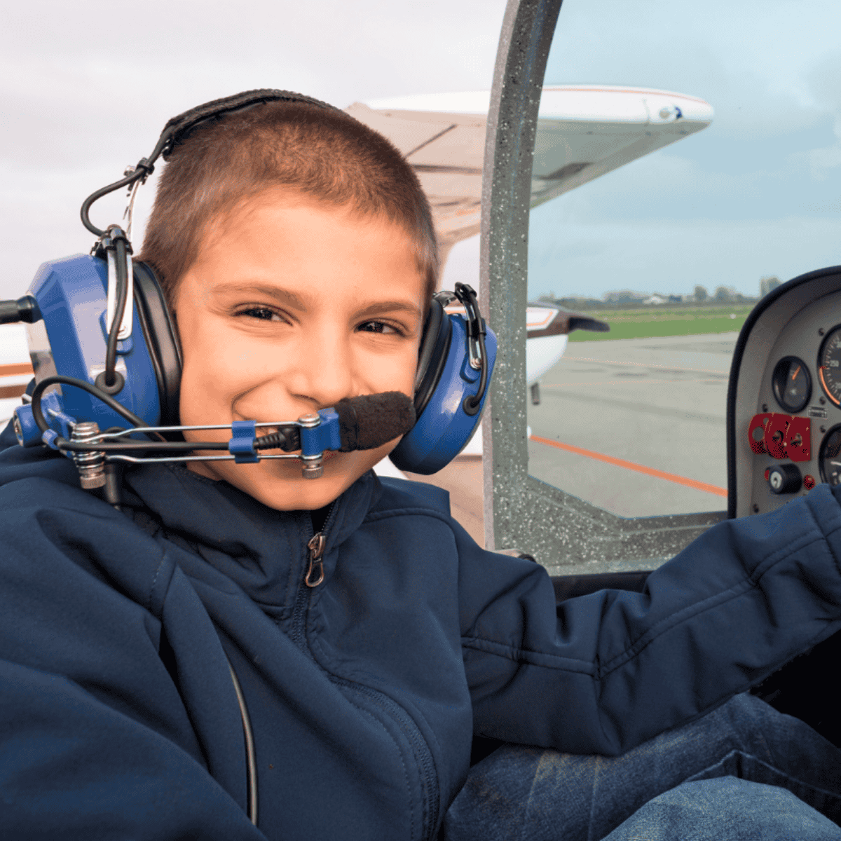 Barn sidder i et militærfly i Værløse Flyhistoriske Hangar omgivet af frivillige formidlere.