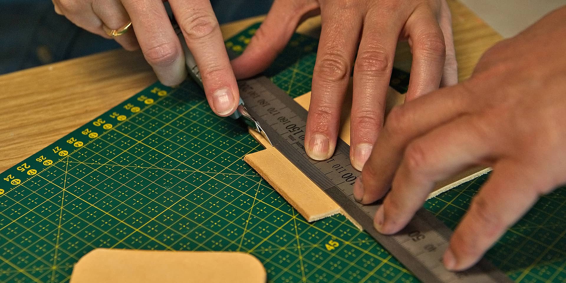 Hænder, lineal, læder og grønt underlag. Fra læderkursus i FOF Aarhus for letøvede