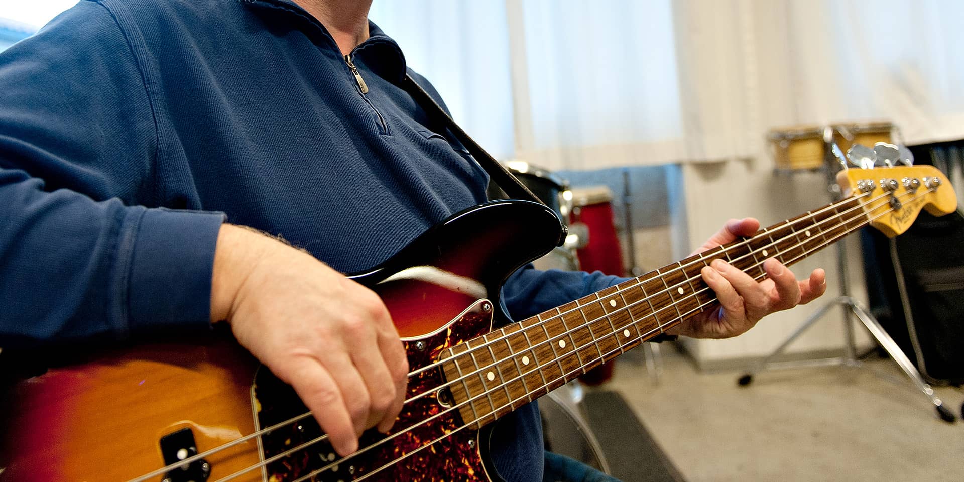 En mand, der spiller bas. Du kan kun se hans overkrop og hånd og bassen. Han har en blå trøje på. Til musikundervisning i FOF Aarhus, på et kursus i bas for begyndere og letøvede.