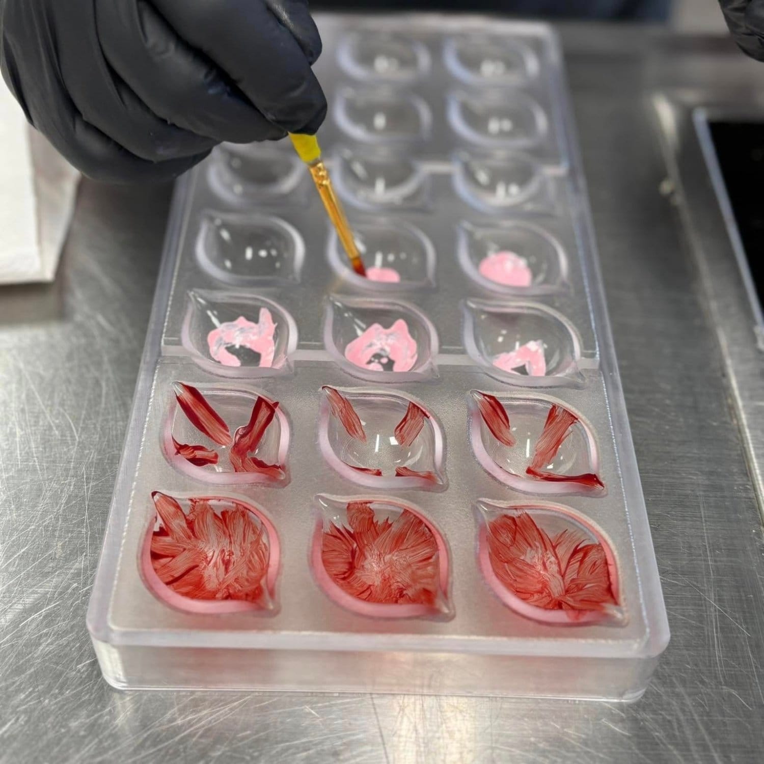 Støbeform til fyldte chokolader, der bliver malet med rød og lyserød