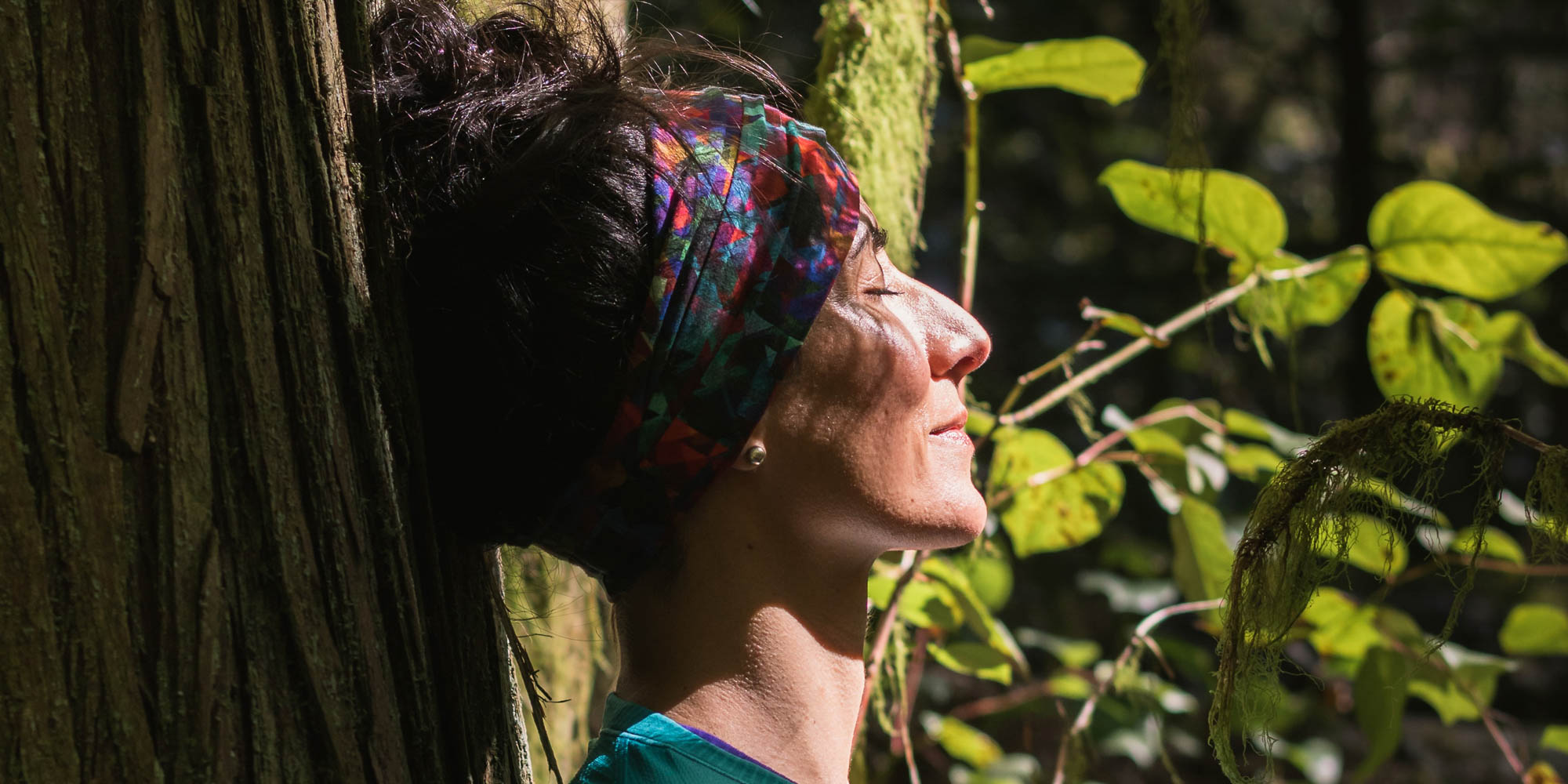 Kvindes ansigt set fra siden omgivet af skov. Selvomsorg i naturen hos FOF København og Nordsjælland.