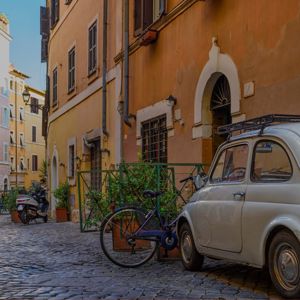 Smalt italiensk gademiljø med gamle bygninger, brostensbelægning og en parkeret klassisk bil og cykel.