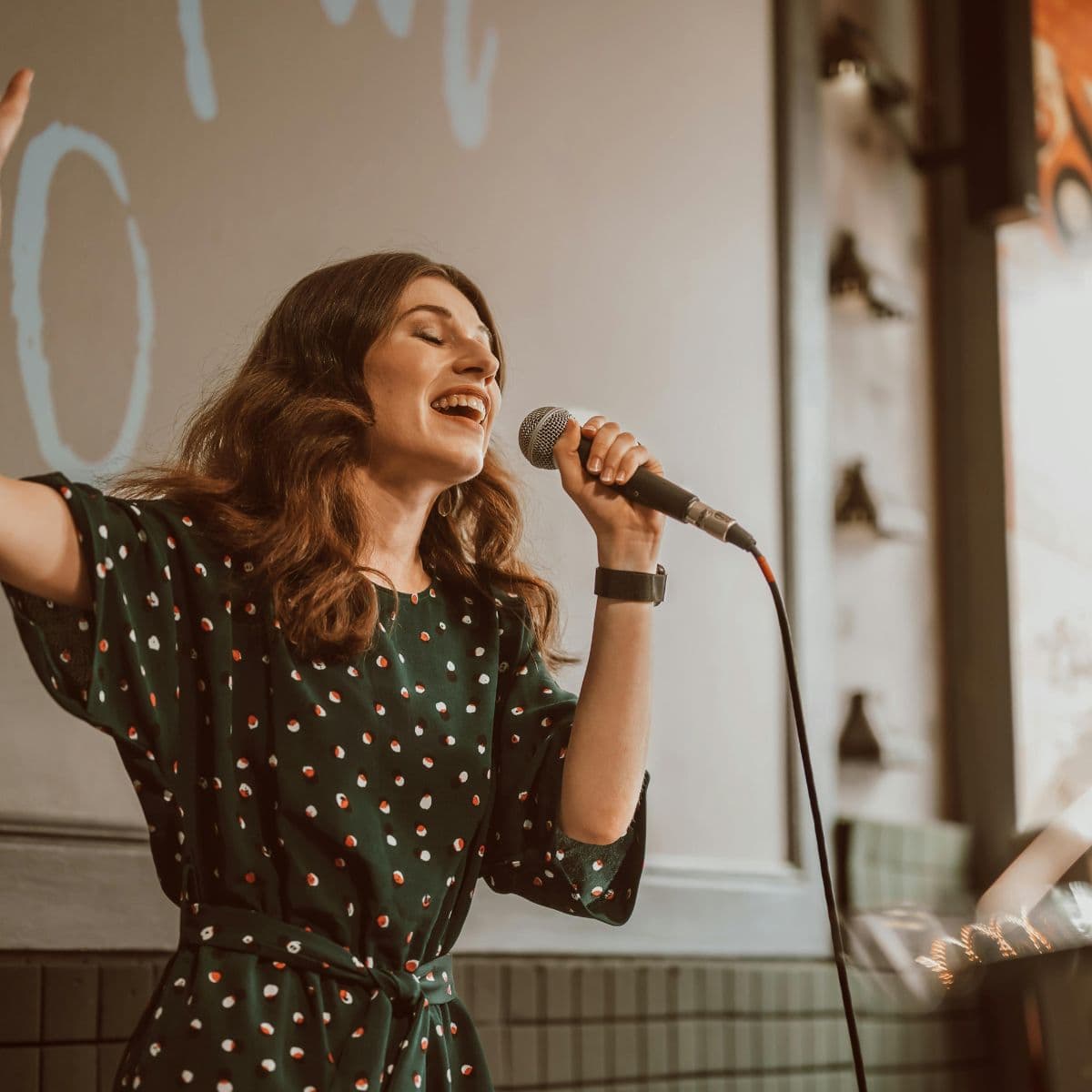 En sangpædagog underviser en gruppe voksne i sangteknik. Deltagerne øver vejrtrækning, klang og dynamik, mens de smilende følger instruktionerne i et lyst øvelokale.