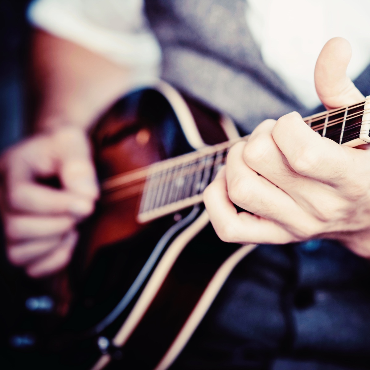 Nærbillede af hænder, der spiller på mandolin – fokus på strenge og greb.