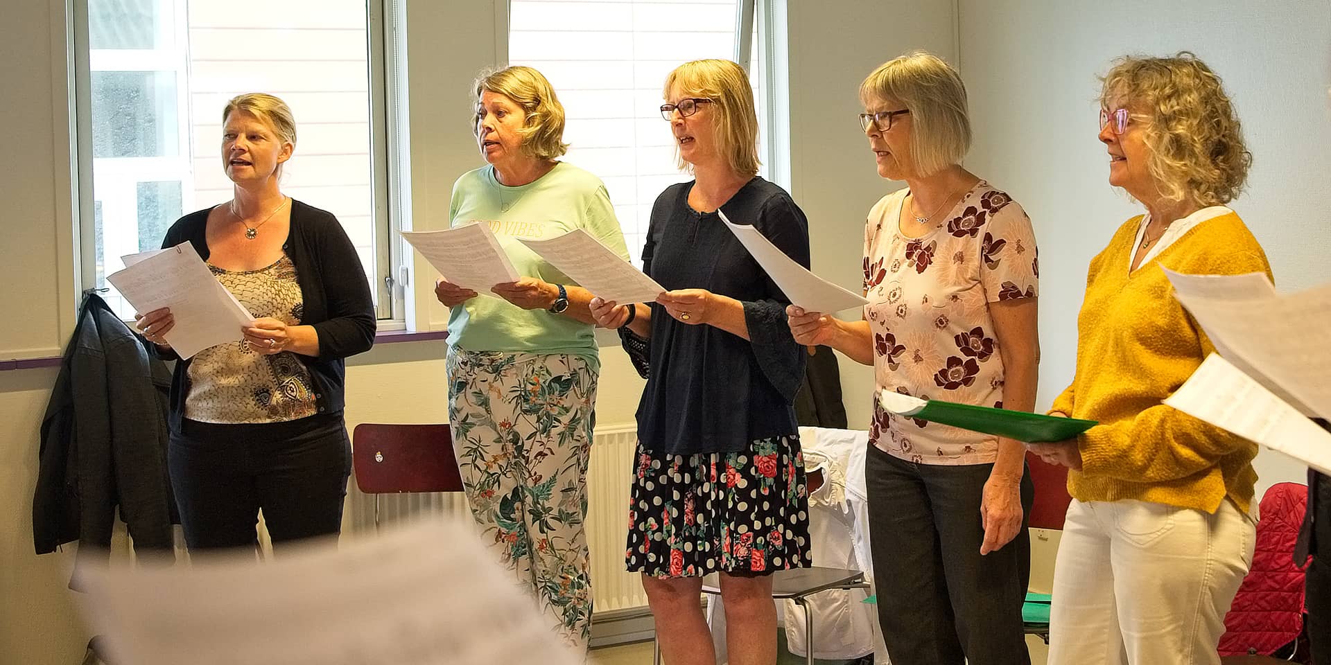 Kvinder, der står med sanghæfte, til sangundervisning for alle på FOF Aftenskolen Aarhus. Sommersang