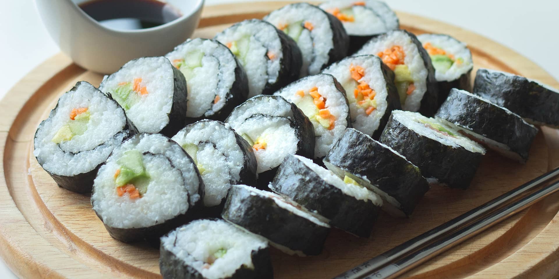 Sushistykker på et træbræt, med spisepinde og skål med soya. Du kan lære at lave sushi på et madlavningskursus i FOF Aarhus.