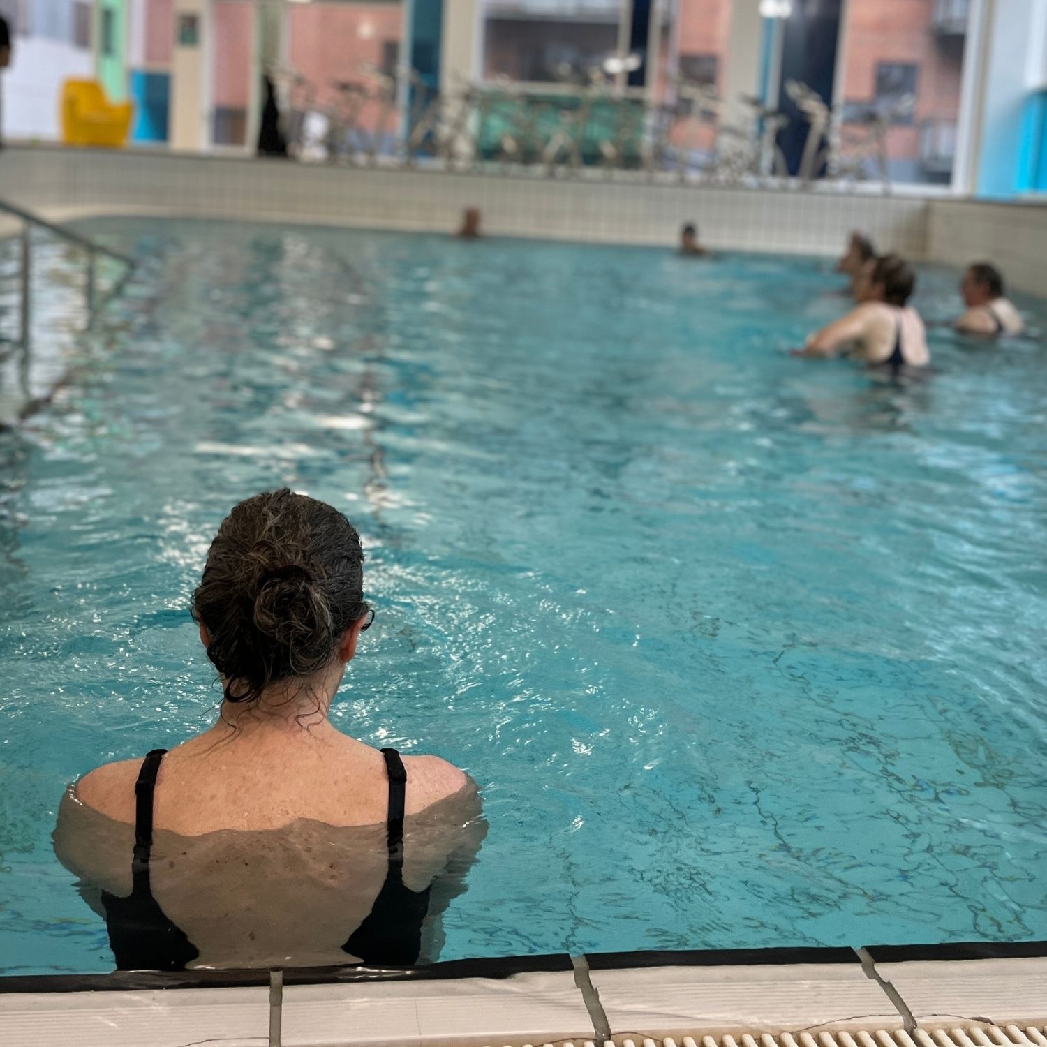 Kursister i vandbassin i en svømmehal iført badetøj