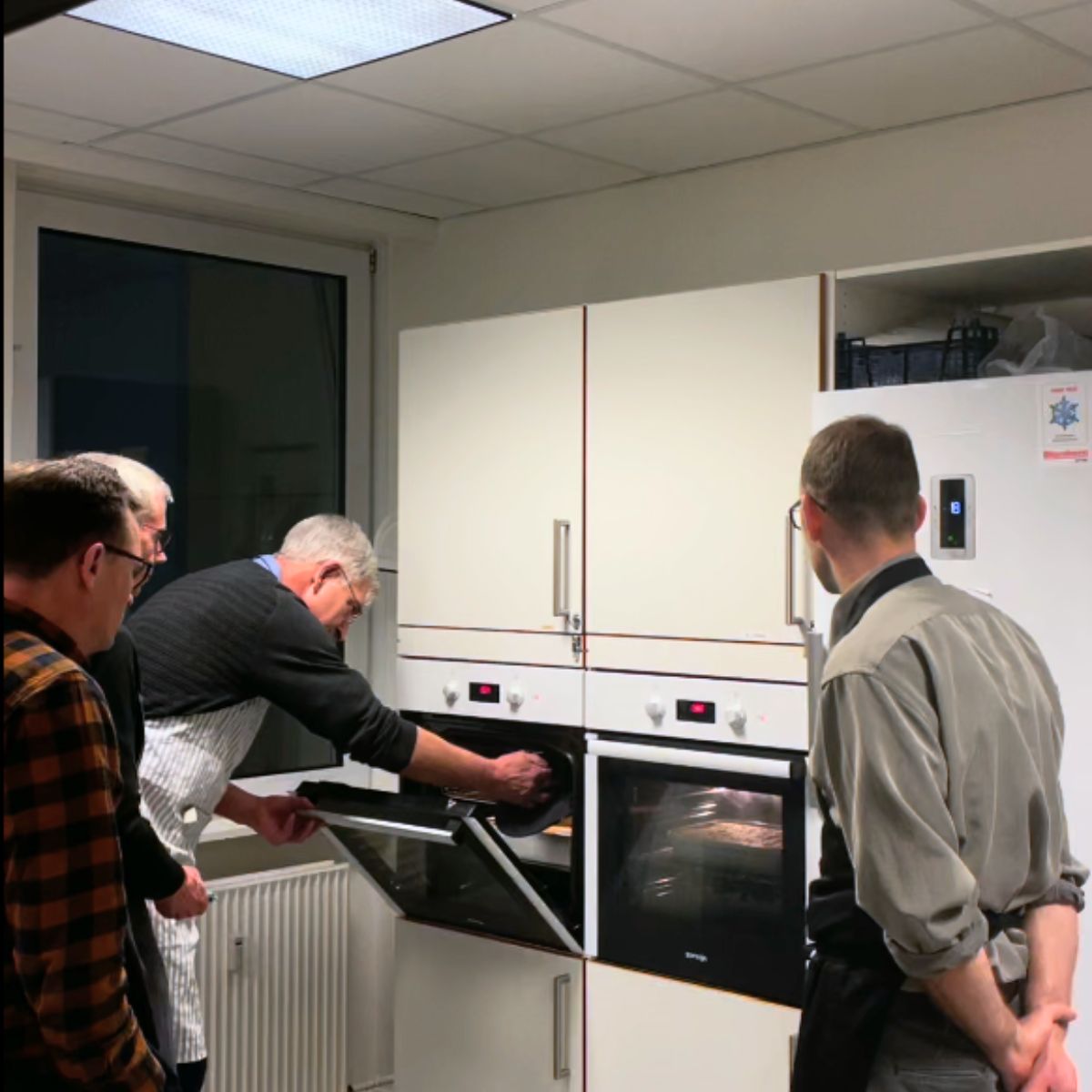 4 mænd det står ved ovnen og holder øje med maden