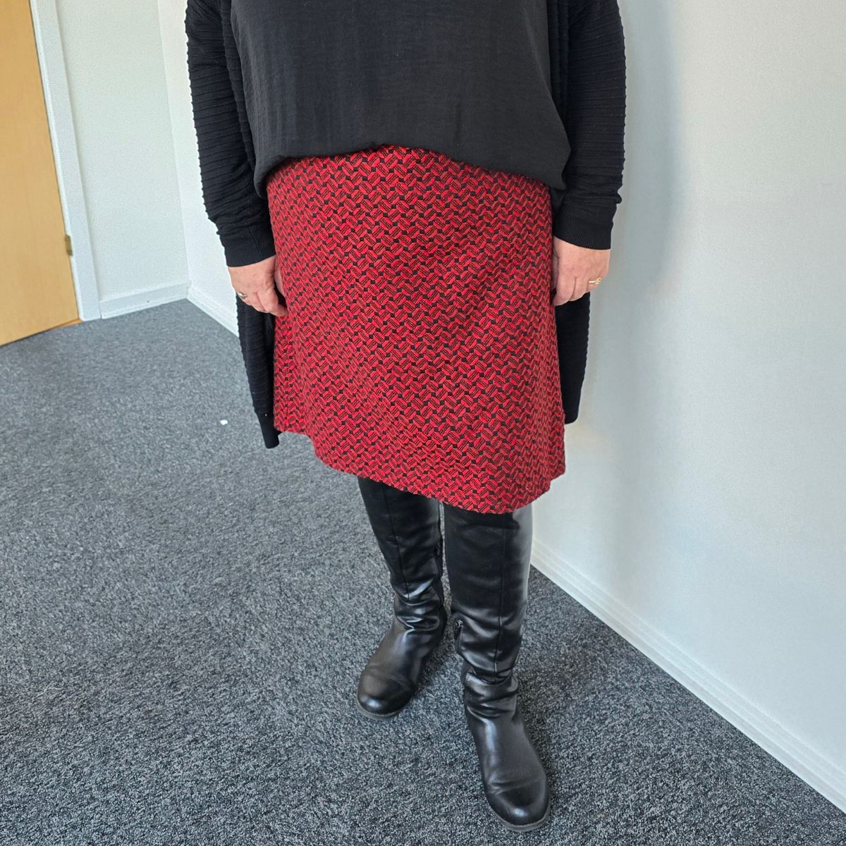 Kvinde står model med sort bluse og rød nederdel