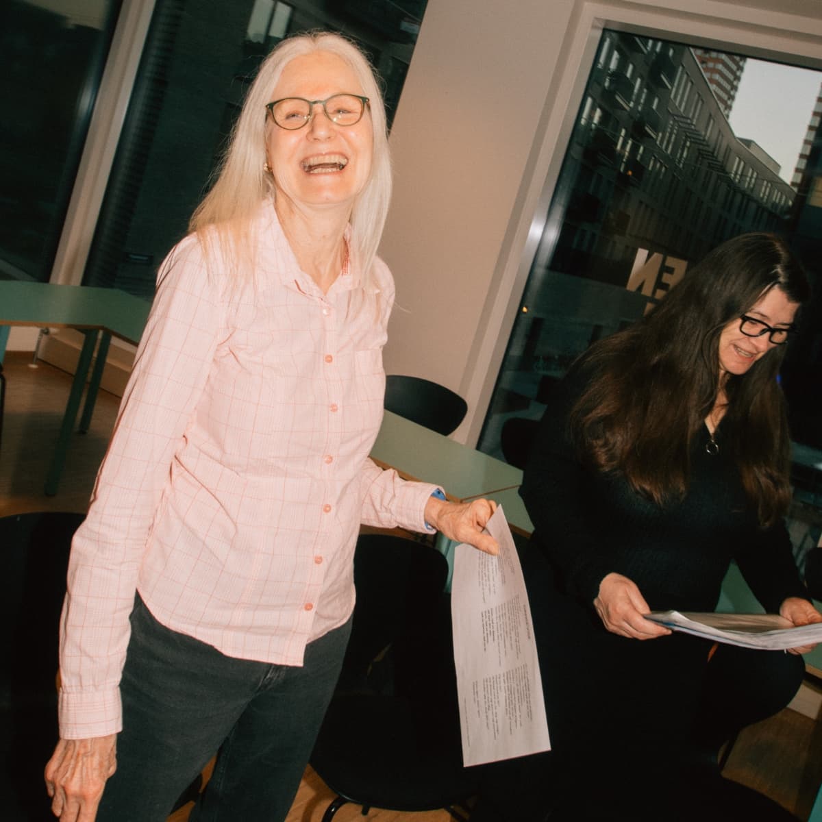 En sangpædagog underviser en gruppe voksne i sangteknik. Deltagerne øver vejrtrækning, klang og dynamik, mens de smilende følger instruktionerne i et lyst øvelokale.