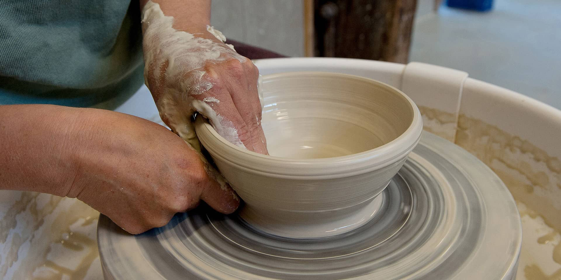 Keramik på en drejeskive og hænder til et keramikkursus, der er hensynstagende, i FOF Aarhus