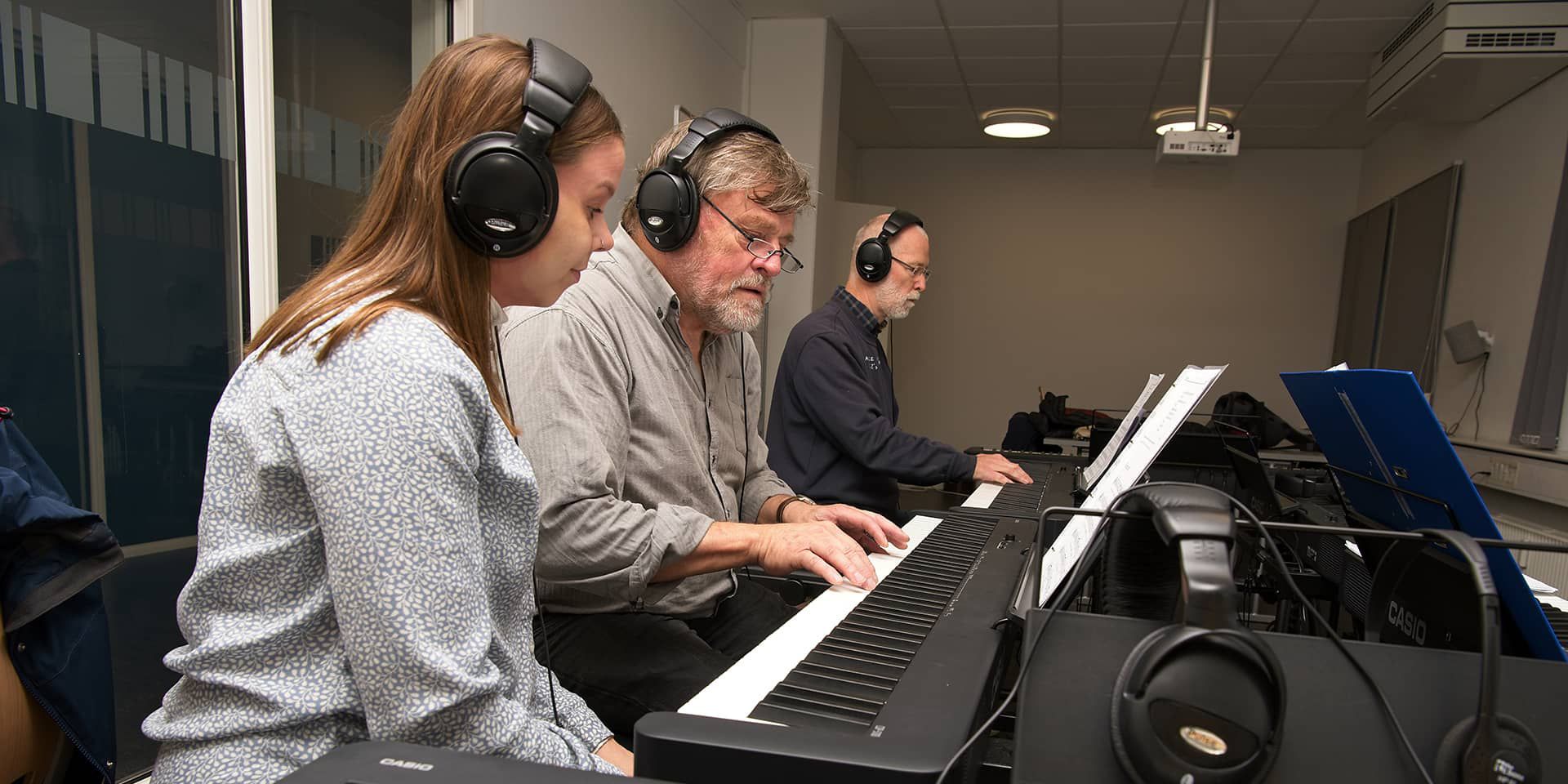 Tre mennesker, der sidder ved klaver. De er til klaverundervisning for begyndere i FOF Aarhus.